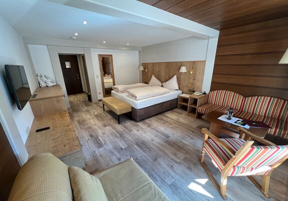 Helles Zimmer mit Holzakzenten, gemütlichem Bett und Sitzbereich mit gestreiften Möbeln.