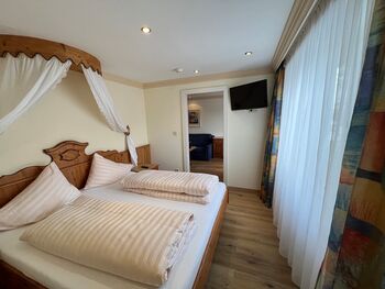 Gemütliches Schlafzimmer mit Himmelbett, Holzmöbeln und großen Fenstern.