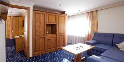 Bright room with wooden furniture, blue couch and carpet, large windows with curtains.