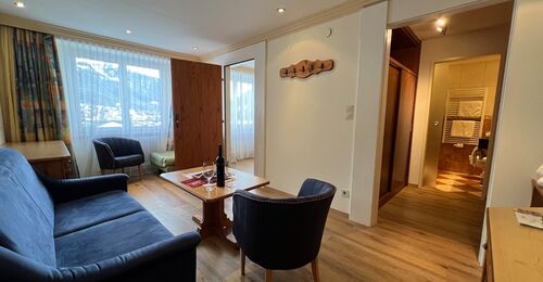 Cozy living room with sofa, armchairs and table, flooded with natural light.