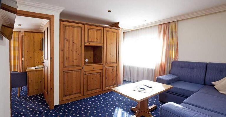 Bright room with wooden furniture, blue couch and carpet, large windows with curtains.