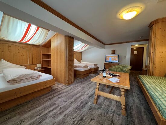 Zimmer mit Holzmöbeln, zwei Betten, Sofas, Tisch, Fernseher und sanfter Beleuchtung.