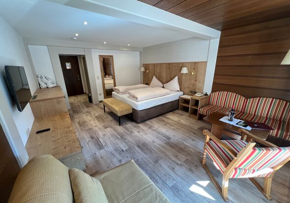 Helles Zimmer mit Holzakzenten, gemütlichem Bett und Sitzbereich mit gestreiften Möbeln.