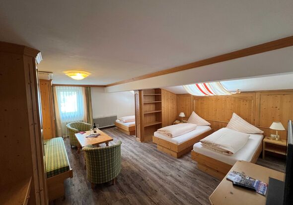 Helles Zimmer mit Holzmöbeln, zwei Betten, Sitzecke und Fenster