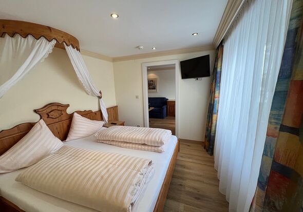 Gemütliches Schlafzimmer mit Himmelbett, Holzmöbeln und großen Fenstern.