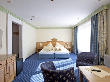 Helles Zimmer mit blauen Akzenten, Doppelbett, Sitzbereich und großen Fenstern.