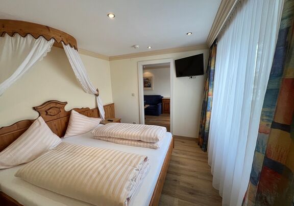 Gemütliches Schlafzimmer mit Himmelbett, Holzmöbeln und großen Fenstern.