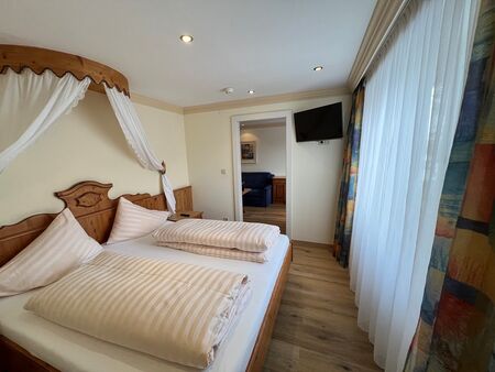 Gemütliches Schlafzimmer mit Himmelbett, Holzmöbeln und großen Fenstern.