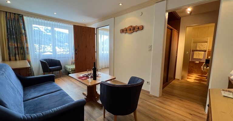 Cozy living room with sofa, armchairs and table, flooded with natural light.