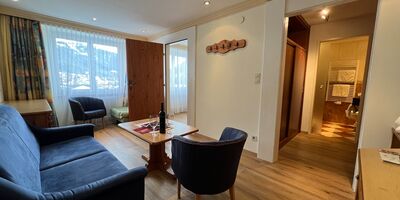 Cozy living room with sofa, armchairs and table, flooded with natural light.