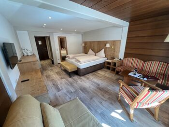 Helles Zimmer mit Holzakzenten, gemütlichem Bett und Sitzbereich mit gestreiften Möbeln.