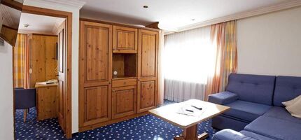 Bright room with wooden furniture, blue couch and carpet, large windows with curtains.