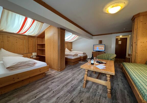 Zimmer mit Holzmöbeln, zwei Betten, Sofas, Tisch, Fernseher und sanfter Beleuchtung.