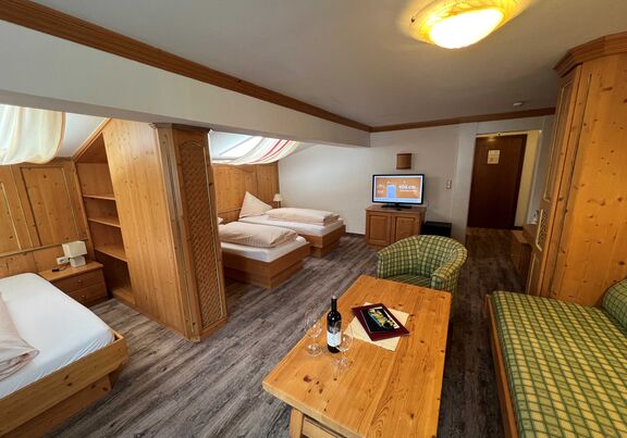 Zimmer mit Holzmöbeln, Fernseher, gemütlichen Betten und Sitzbereich für entspannte Aufenthalte.