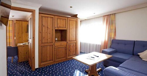 Bright room with wooden furniture, blue couch and carpet, large windows with curtains.