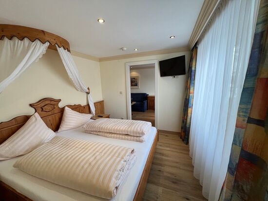 Gemütliches Schlafzimmer mit Himmelbett, Holzmöbeln und großen Fenstern.