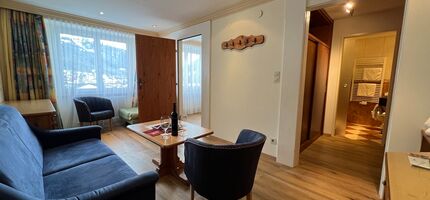Cozy living room with sofa, armchairs and table, flooded with natural light.