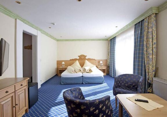 Helles Zimmer mit blauen Akzenten, Doppelbett, Sitzbereich und großen Fenstern.