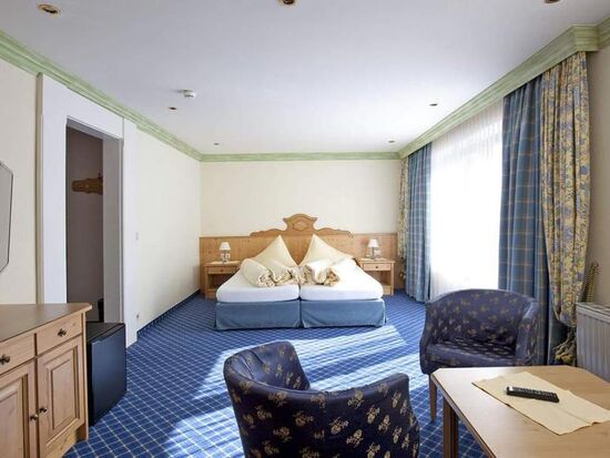 Helles Zimmer mit blauen Akzenten, Doppelbett, Sitzbereich und großen Fenstern.