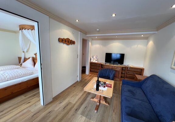 Elegantes Wohnzimmer mit blauer Couch, Holzdetails und angrenzendem Schlafzimmer.