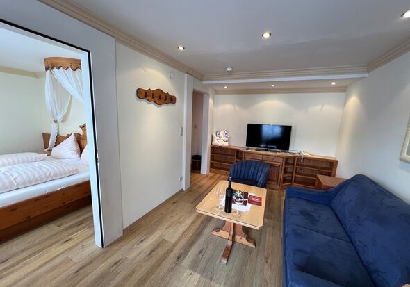 Elegantes Wohnzimmer mit blauer Couch, Holzdetails und angrenzendem Schlafzimmer.