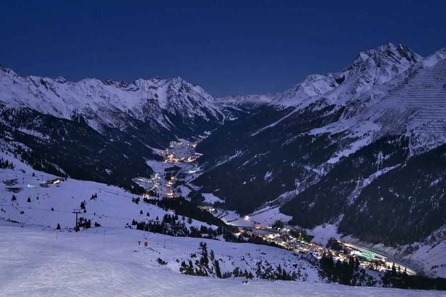 Snow-covered mountains under a clear night sky with lights in the valley.