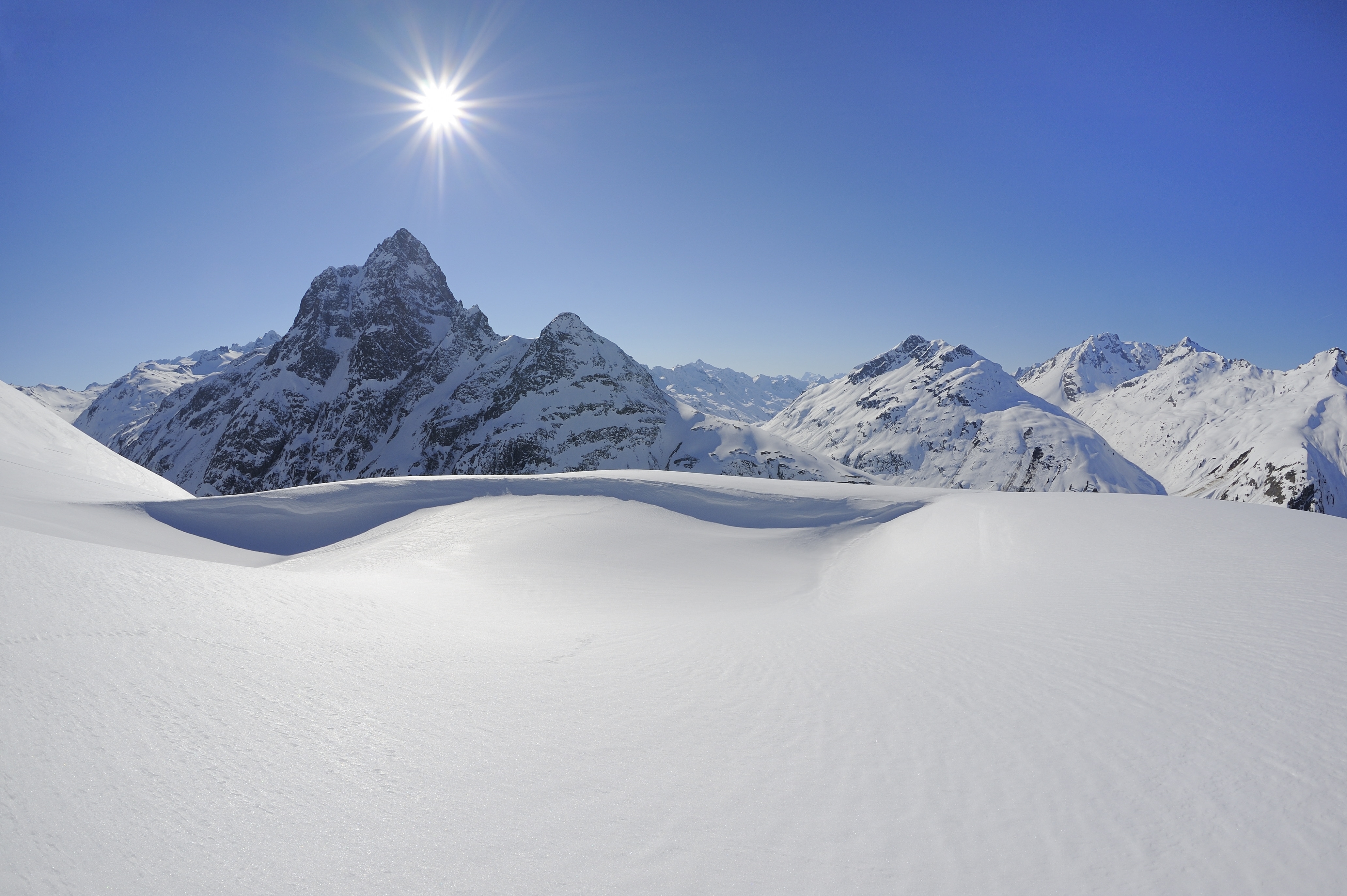 Snow-covered mountain landscape under bright sunshine and a clear blue sky.